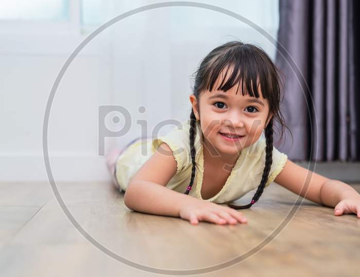 Portrait Of Cute Little Girl Lying On Floor With Barefoot And Looking At Camera At Home. People Lifestyles Concept.