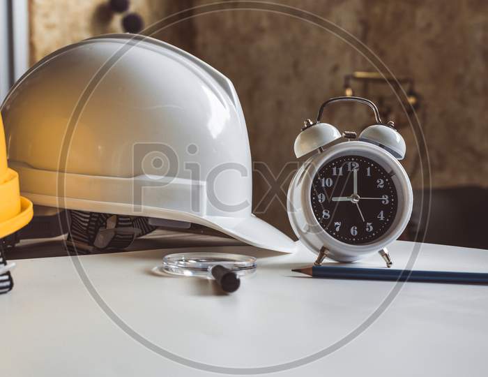 Close Up Of Clock And Engineering Safety Helmet On Blueprint Table. Architecture And Engineering Equipment Concept. Construction Site And Occupation Job Of Interior Building Professional Theme.