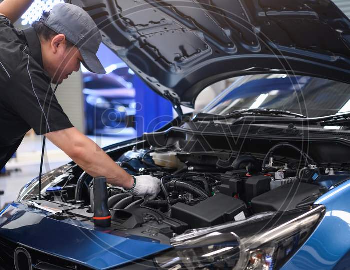 Asian Male Auto Mechanic Examine Car Engine Breakdown Problem In Front Of Automotive Vehicle Car Hood. Safety Technical Inspection Care Check Service Maintenance For Customer Before Long Road Trip