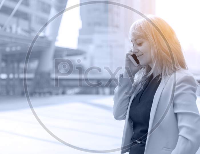 Businesswoman Making Conversation With Cell Phone.  Business And Communication Concept. Technology And Lifestyle Concept City And Urban Theme. Happy Life At Outdoors Theme. Blue Tone Filter