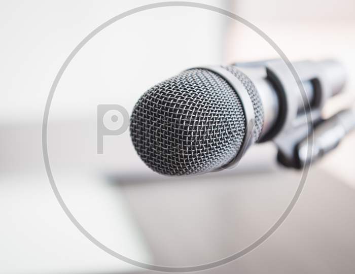 Closeup Of Microphone In Lecture Room Background Speech In Seminar Convention Hall Room. Mic Speaker Of Teacher On Podium In College Or University. Workshop Event And Entertainment Broadcast Concept.