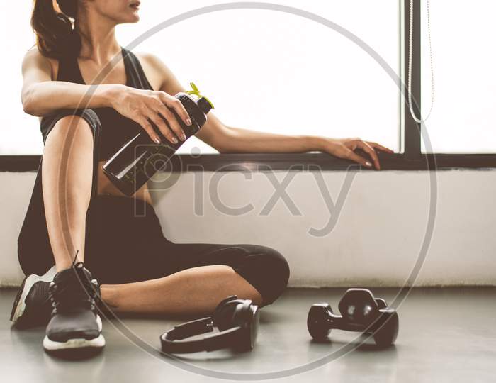 Woman With Dumbbell And Device Exercise Lifestyle Workout In Gym Fitness Breaking Relax After Sport Training With Protein Shake Bottle Background. Healthy Lifestyle Bodybuilding And Athlete Muscles