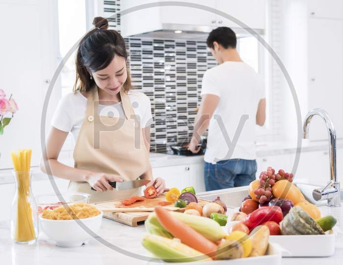 Asian Lovers In Kitchen. Woman Slice Vegetables And Cooking, Man Making Spaghetti, Couple And Family Concept. Honeymoon And Holidays Theme