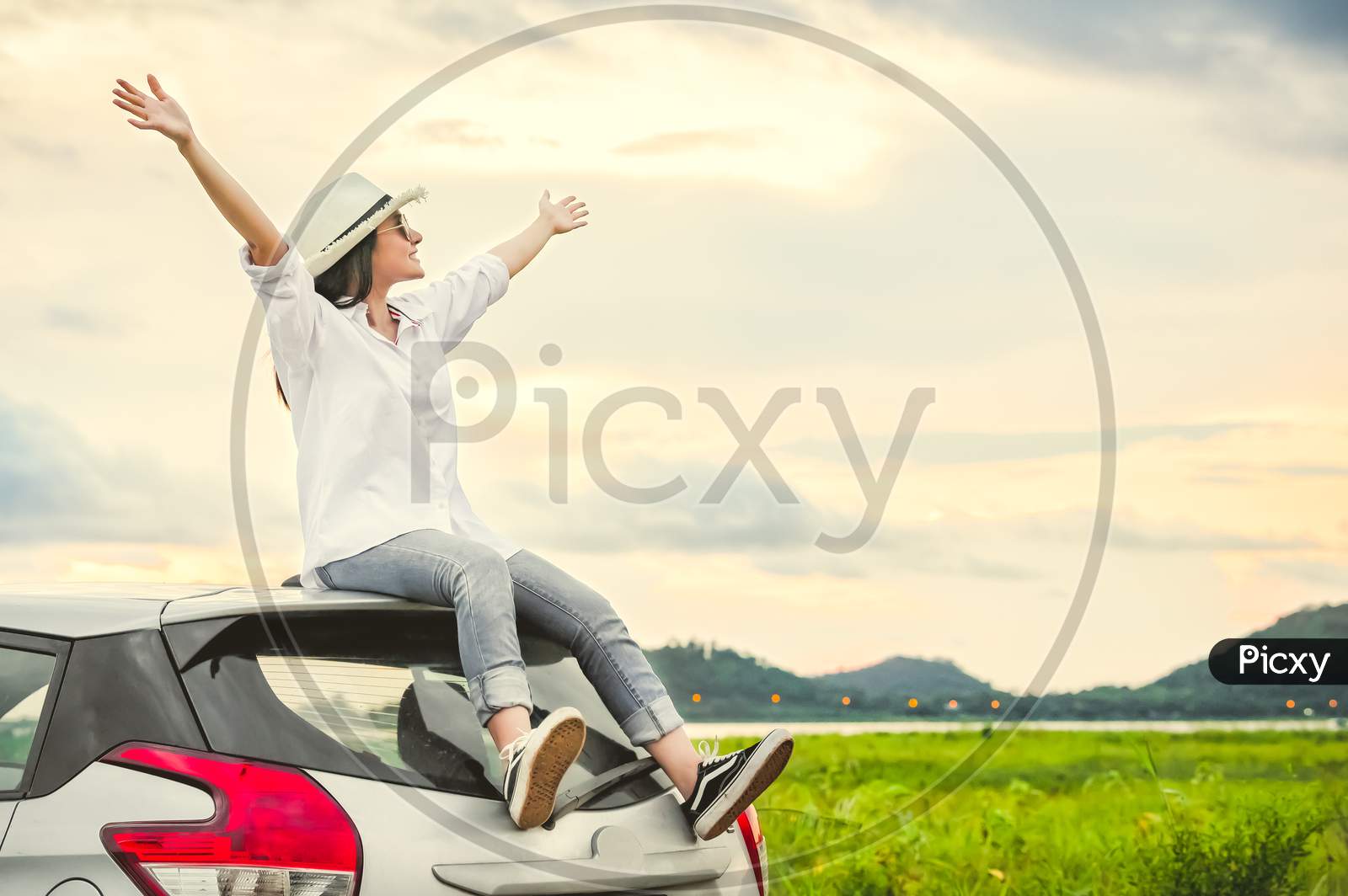 Happy Asian Woman Spread Arms Widely And Breathed Fresh Air With Happiness Mood In Evening After Sunset On Car Roof. People Lifestyle In Long Vacation Trip Concept. Outdoors Nature And Transportation
