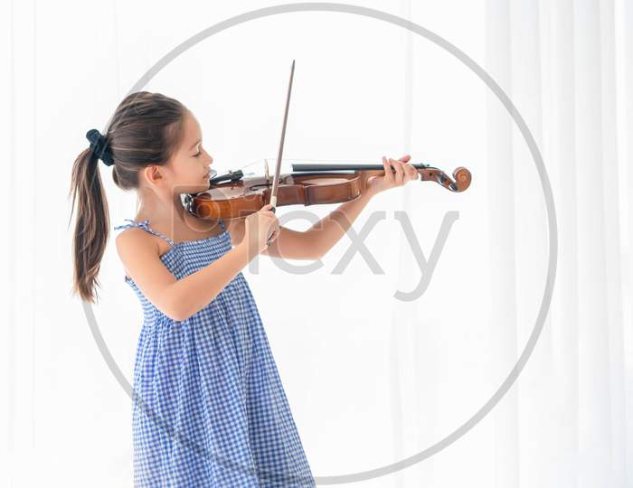 Cute Little Girl Playing Violin In Bedroom With White Curtain Background. Musical And People Lifestyle. Education And Recreation Concept. Asian Musician Violinist Kids Doing Hobby And Leisure At Home.