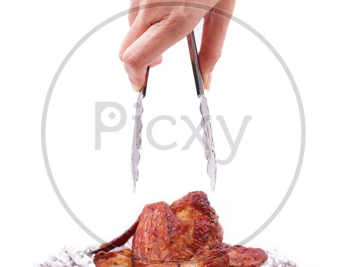 Hand Holding Serving Roasted Chicken In Aluminum Foil With Tongs. Food And Appetizer Concept. Kitchen And Cooking Theme. Delicious Grilled Leg And Wing On Isolated White Background