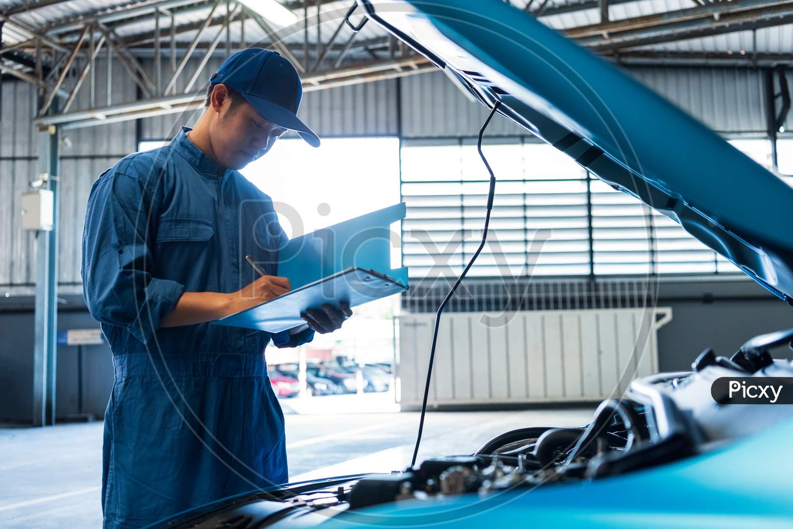 Car Mechanic Holding Clipboard And Checking To Maintenance Vehicle By Customer Claim Order In Auto Repair Shop Garage. Engine Repair Service. People Occupation And Business Job. Automobile Technician