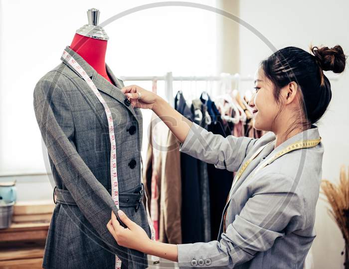 Asian Female Fashion Designer Girl Making Fit On The Formal Suit Uniform Clothes On Mannequin Model. Fashion Designer Stylish Showroom. Sewing And Tailor Concept. Creative Dressmaker Stylist.
