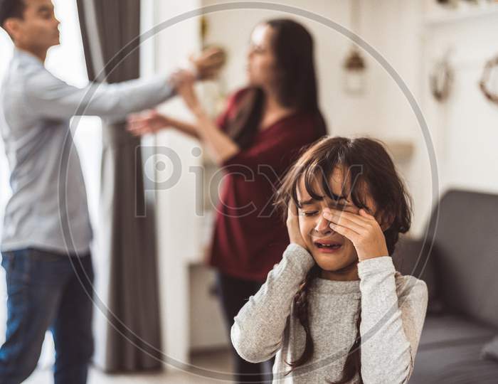 Little Girl Crying Because Of Her Parents Quarreling. Girl Abused With Mother And Father Shouting And Conflict Angry Background In Home. Family Dramatic Scene, Family Social Issues Problem Concept.