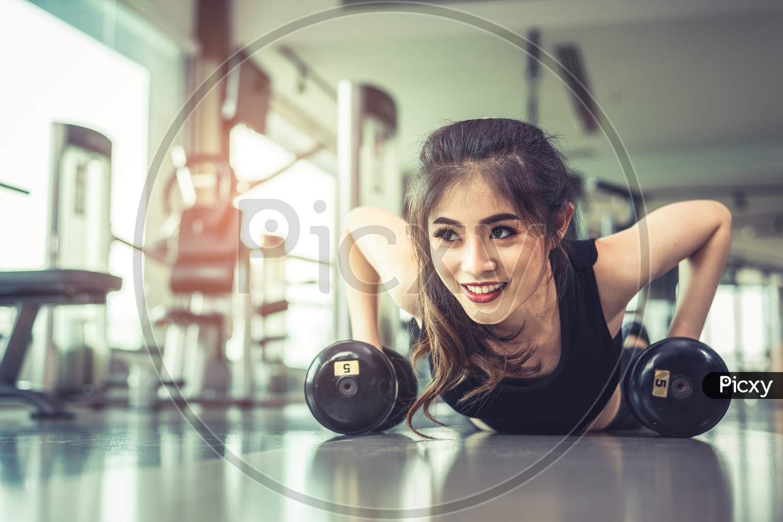 Asian Young Woman Doing Push Ups With Dumbbell On Floor In Fitness Gym And Equipment Background. Workout And Sport Exercise Concept. Healthy And Happiness Concept. Beauty And Body Build Up Theme.