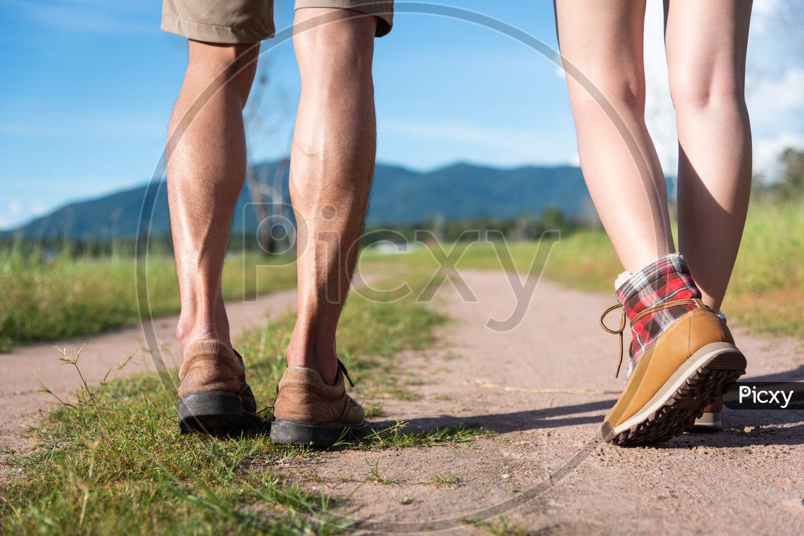 Close Up Of Lower Legs Of Two Travelers Walking Along Path In Nature. Hiking And Camping Concept. Backpacker An Tourist Concept. Outdoors Activity And Adventure Theme.