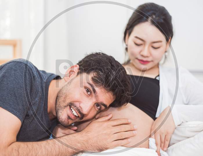 Father Hearing His Son Or Daughter Kicking Sound Check Inside Mother Belly When Sitting On Lying On Bed At Home. Family Healthy And Couples Concept. Happy Sweet Home Honeymoon And Wedding Theme