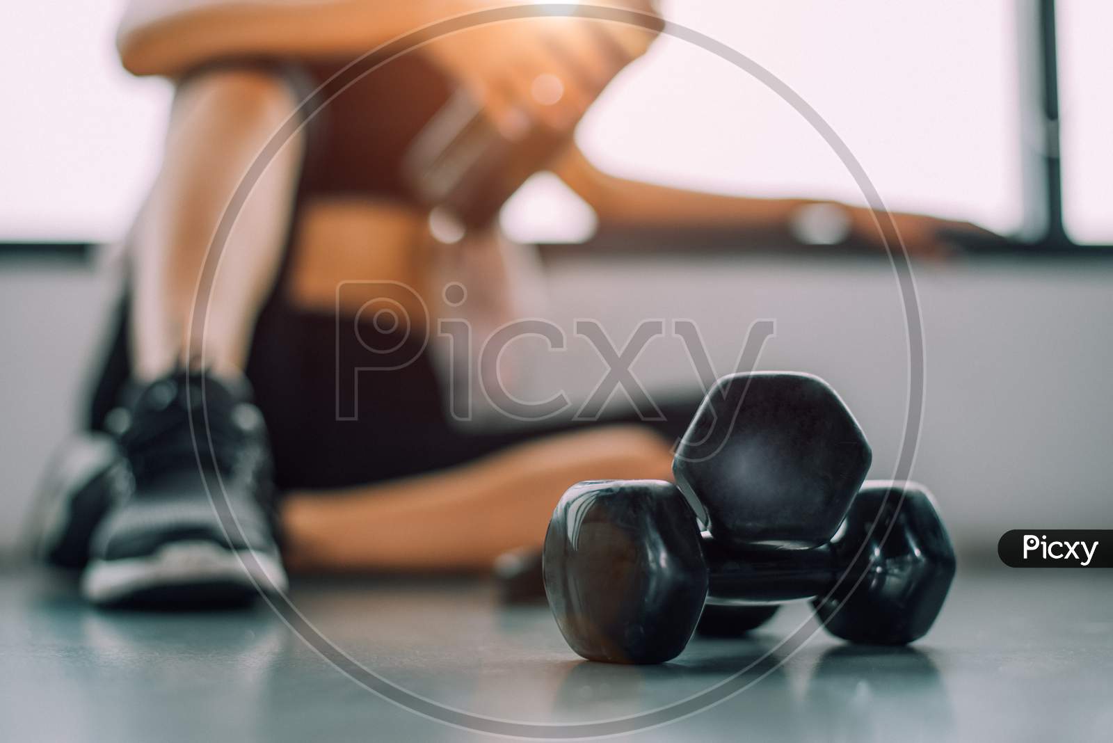 Close Up Of Dumbbell With Exercise Woman Lifestyle Workout In Gym Fitness Breaking Relax After Sport Training With Protein Shake Bottle Background. Healthy Lifestyle Bodybuilding Athlete Muscles