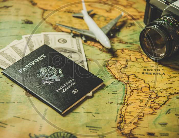 Tourist Planning Props And Travel Accessories With American Passport, Airplane, Digital Camera And Us Dollar Banknote Money On Old Grunge Style Map. Holiday And Vacation. Tourism Long Weekend Concept.