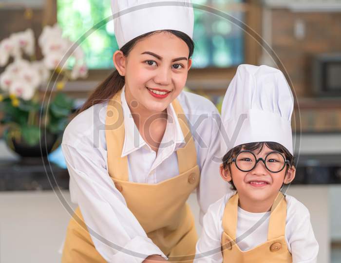 Portrait Of Beautiful Asian Woman And Cute Little Boy With Eyeglasses Prepare To Cooking In Kitchen At Home. People Lifestyles And Family. Homemade Food And Ingredients. Two Thai People Looking Camera
