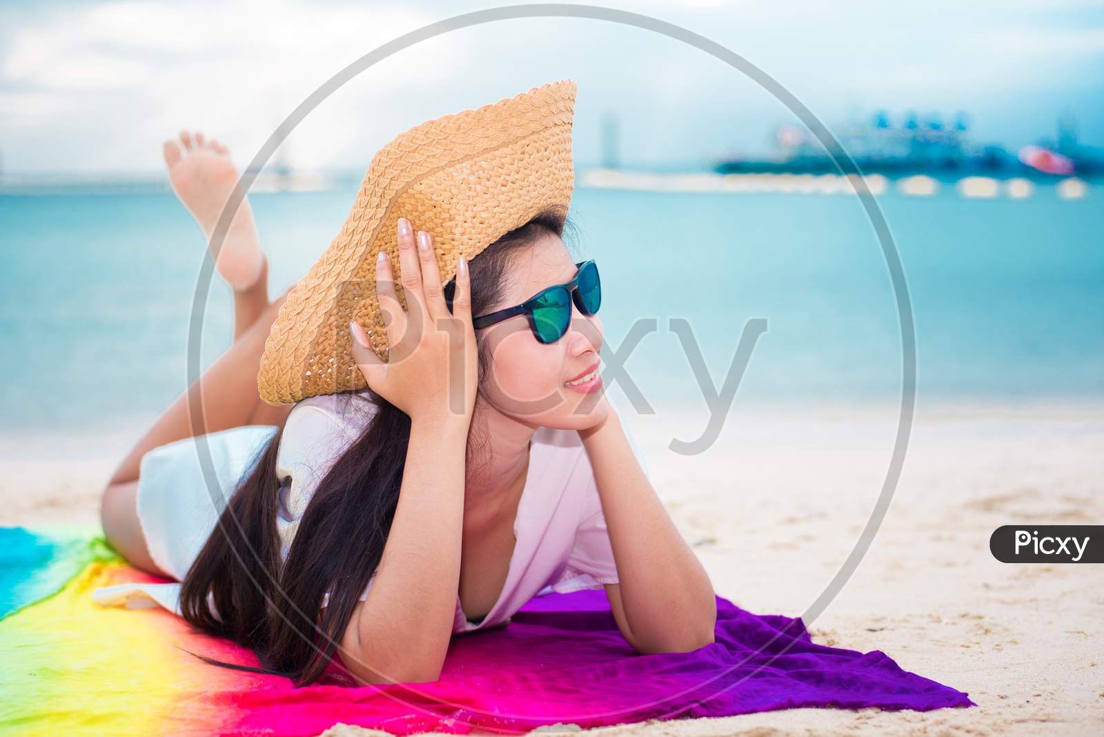 Asian Woman In Casual And Straw Hat Lying On Tropical Beach With Sea Background. Relax And Lifestyle Concept. Holiday And Vacation Concept. Single Woman And Happiness Theme.