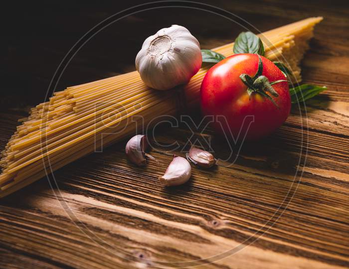 Tasty Appetizing Italian Spaghetti Pasta Ingredients For Kitchen Cuisine With Tomato, Garlic And Basil On Wooden Brown Table. Food Meal And Italian Recipe Homemade. Top View Abgle Above