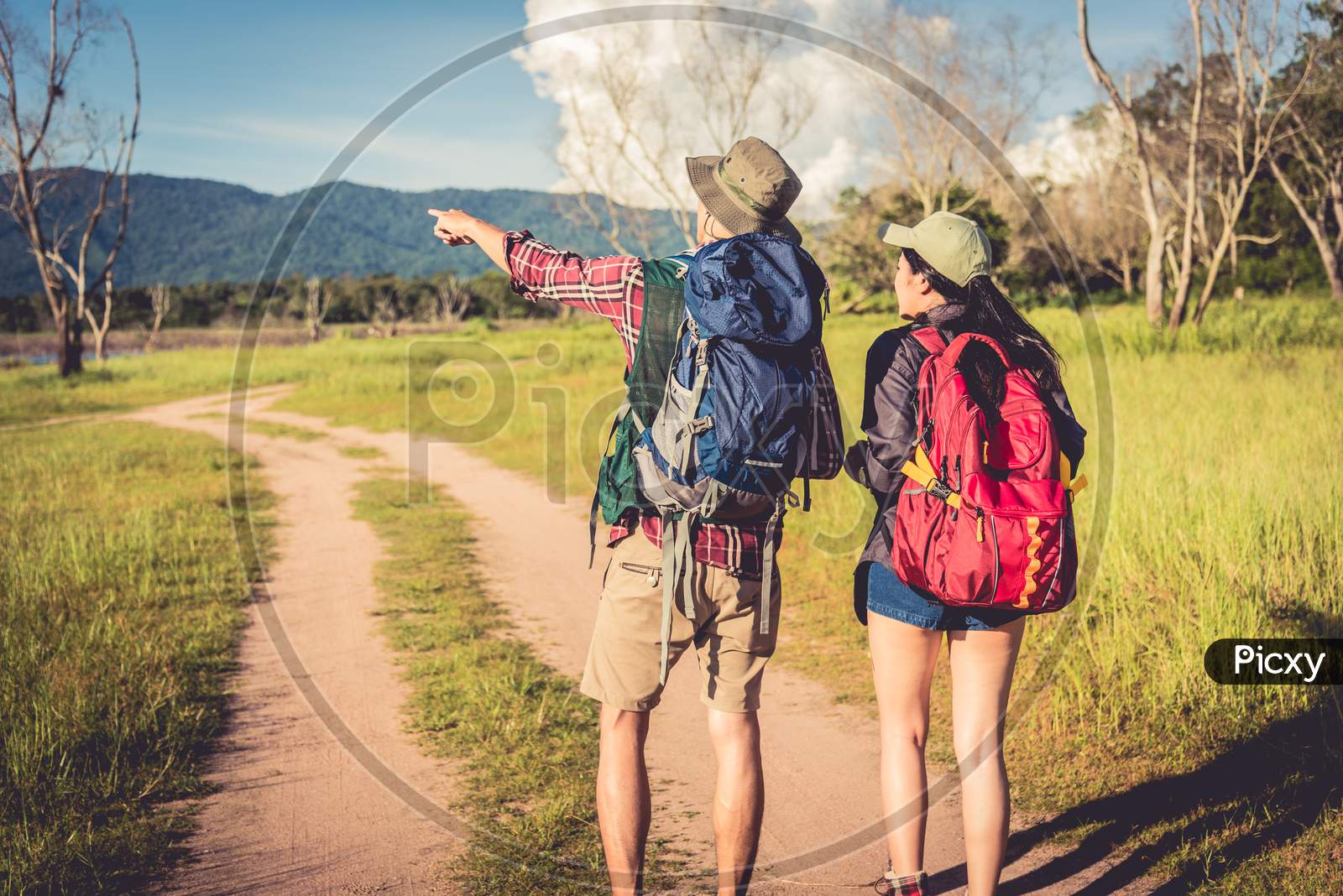 Two People Walking On Path In Meadow Field. Male And Female Traveler Looking At Attraction View Point. Couples Adventure At Outdoors Together. People And Lifestyles Concept. Trip And Camping Theme.