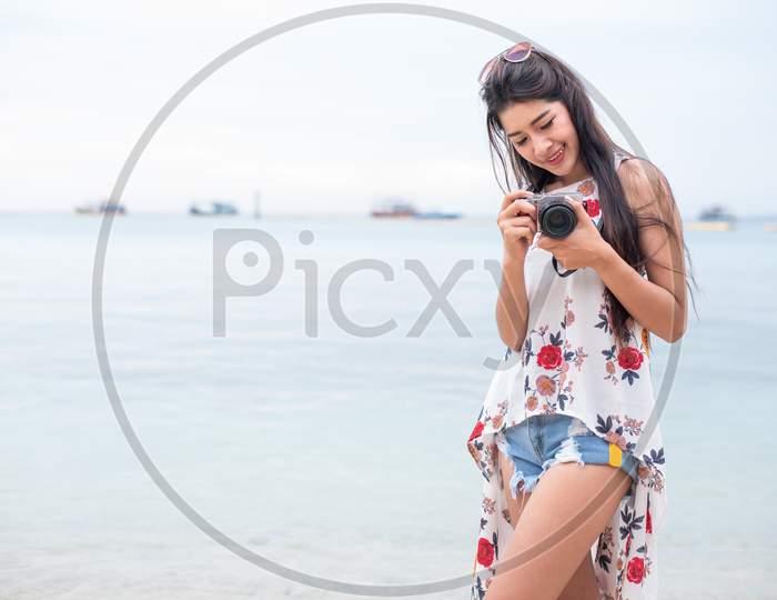 Asian Woman Enjoy Take Photo By Digital Camera At Beach. Single And Lonely Woman Concept. Happiness And Lifestyle Concept. Beauty And Nature Theme. Ocean And Sea Background. Technology And Woman Day