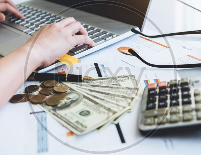 Close Up Of Working Woman Hand Using Laptop Computer On Office Desk With Money Report Paper Eyeglasses And Calculator. Business And People Lifestyles. Financial And Economy Investment. Work From Home