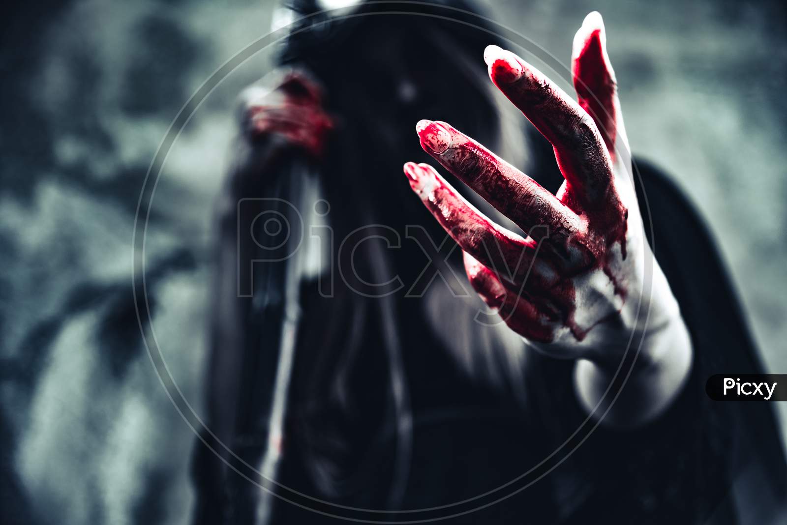 Witch Showing Bloody Hand. Female Demon Angel In Black Clothes And Hood On Grunge Wall Background. Halloween Day And Mystery Concept. Fantasy Of Magic Theme. Afterlife And Death Concept.
