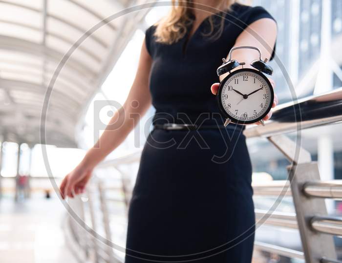 Business Women Show Alarm Clock And Shocked With Late In Rush Hours When Going To Work In City Urban Background. Deadline And Wake Up Late. People Lifestyle And Daily Life Planner Concept.