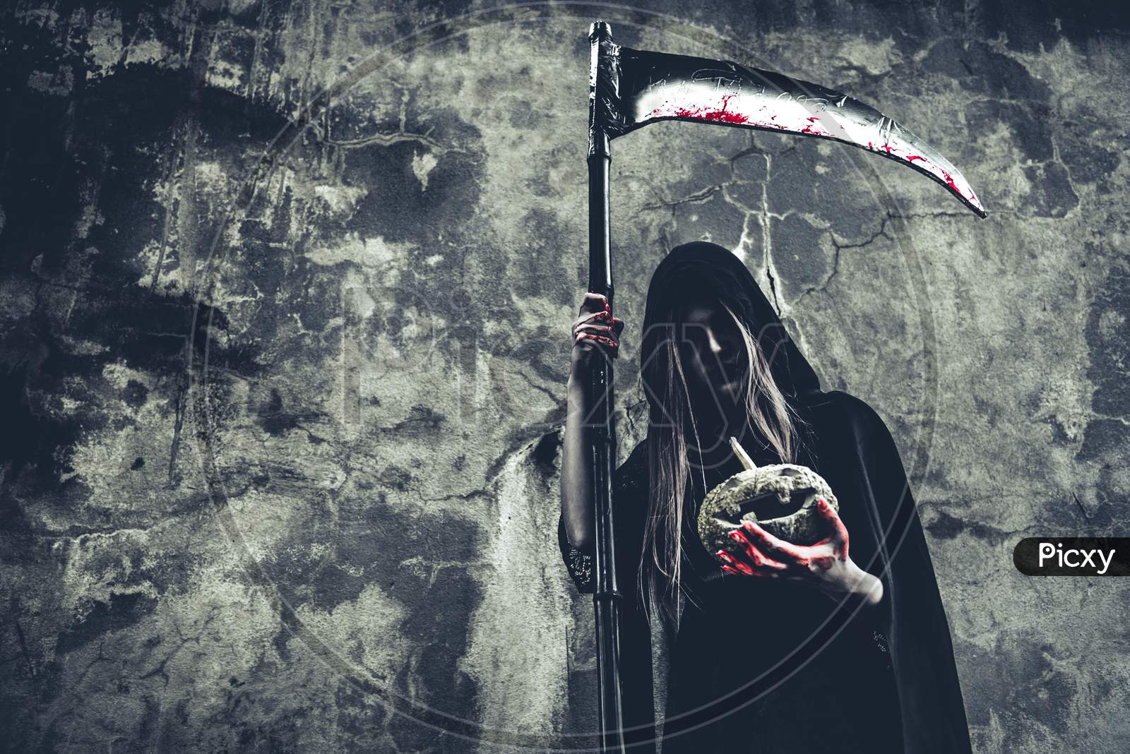 Demon Witch Holding Pumpkin In Hand With Bloody Reaper On Grunge Wall Background. Halloween And Religious Concept. Demon Angel And Satan Theme.