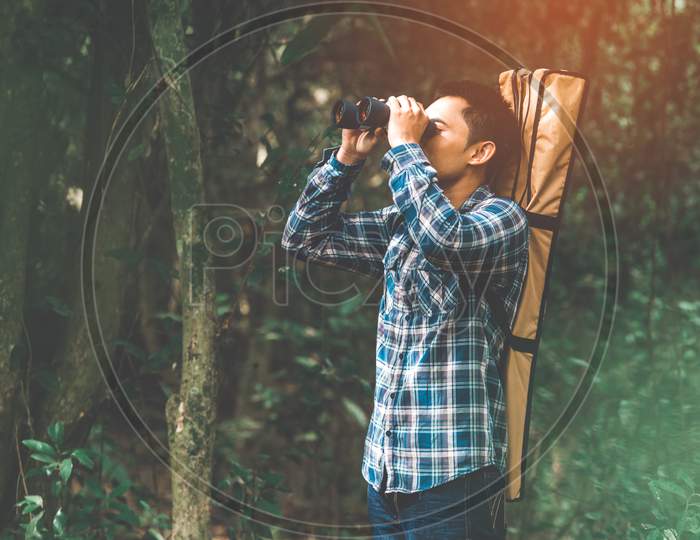 Man With Binoculars Telescope In Forest Looking Destination As Lost People Or Foreseeable Future. People Lifestyles And Leisure Activity Concept. Nature And Backpacker Traveling Jungle Background