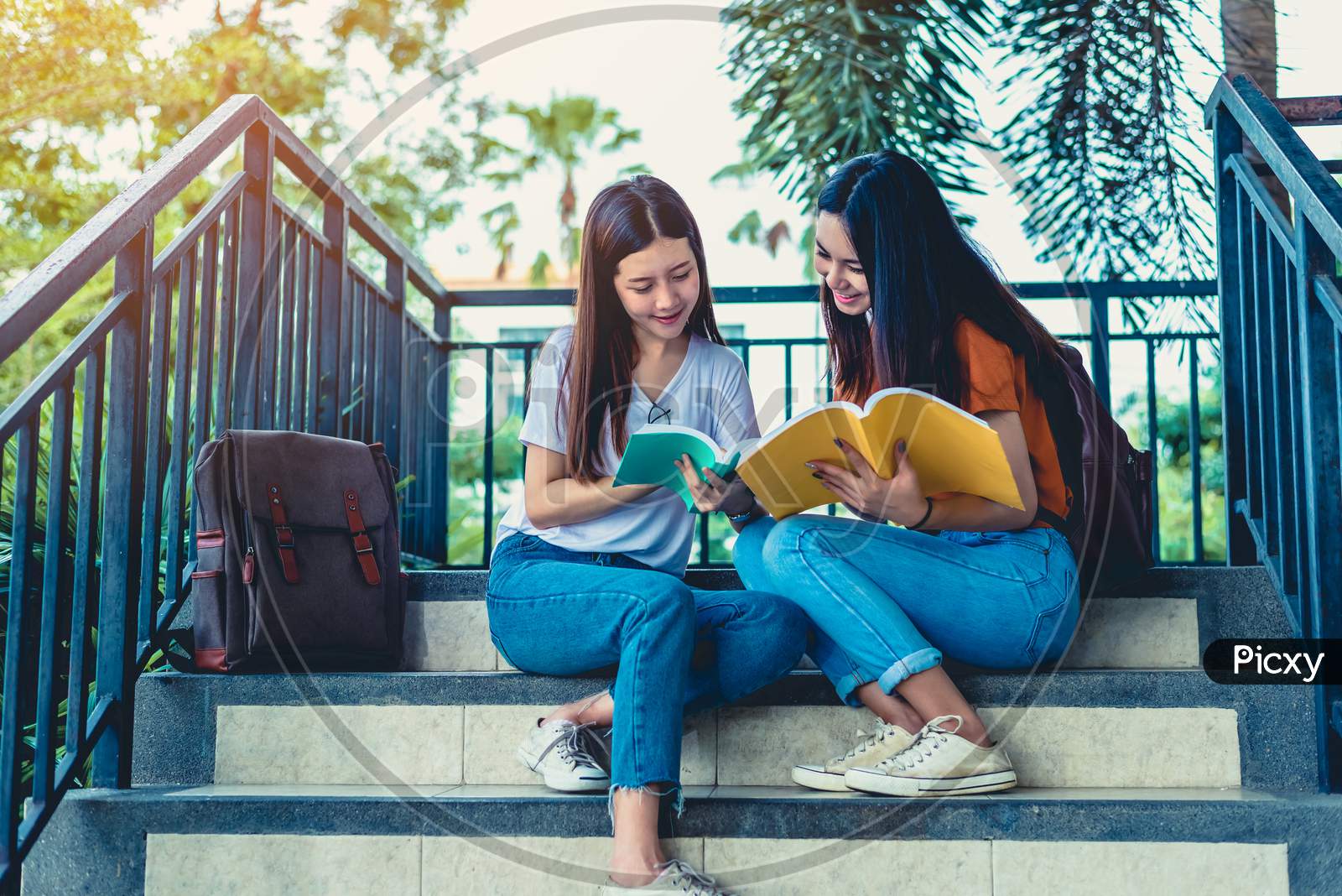 Two Asian Beauty Girls Reading And Tutoring Books For Final Examination Together. Student Smiling And Sitting On Stair. Education And Back To School Concept. Lifestyles And People Portrait Theme.