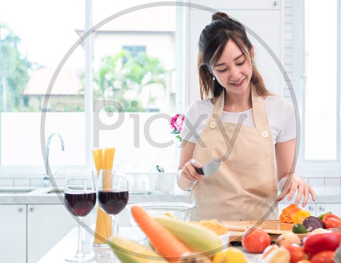 Asian Beauty Woman Cooking And Slicing Vegetable In Kitchen Room With Full Of Food And Fruit On Table. Holiday And Happiness Concept. People And Lifestyles Concept. Family And Dinner Party Theme.