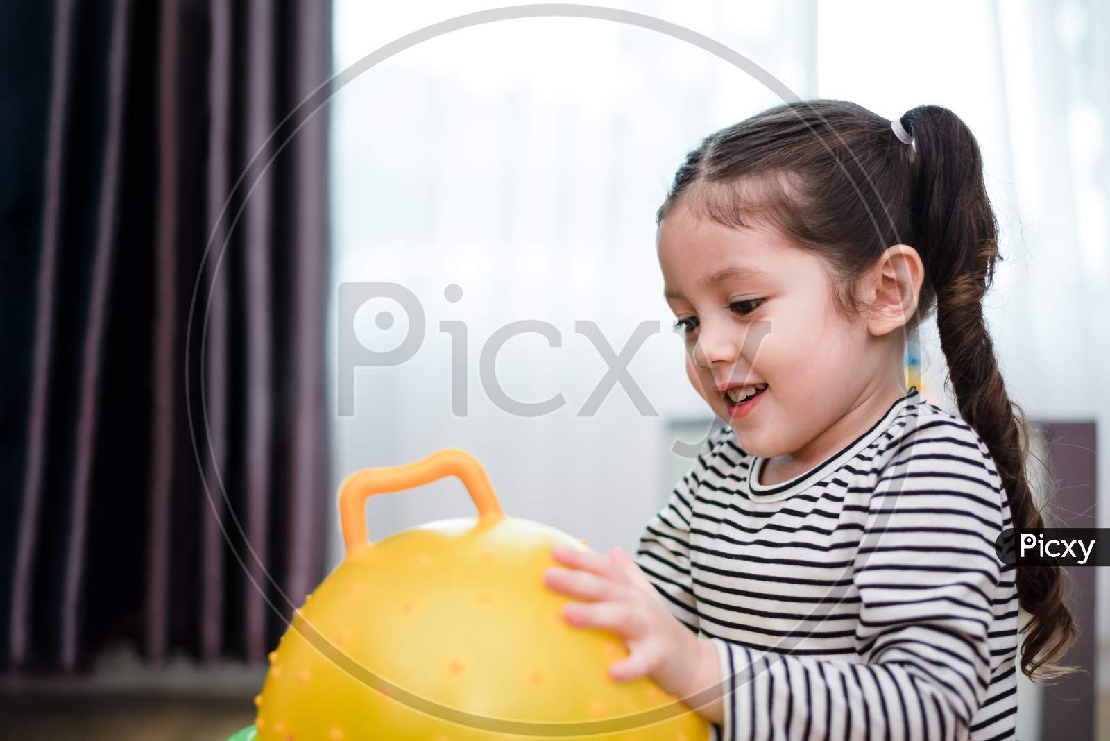 Little Girl Playing Rubber Ball In Home. Education And Happiness Lifestyle Concept. Funny Learning And Children Development Theme.