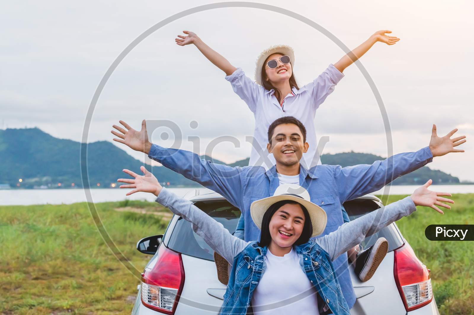 Happy Asian Friends Spread Arms Widely And Breathed Fresh Air With Happiness Mood In On Raod Trip In Car Trunk. People Lifestyle In Long Vacation Trip Concept. Outdoors Nature And Transportation