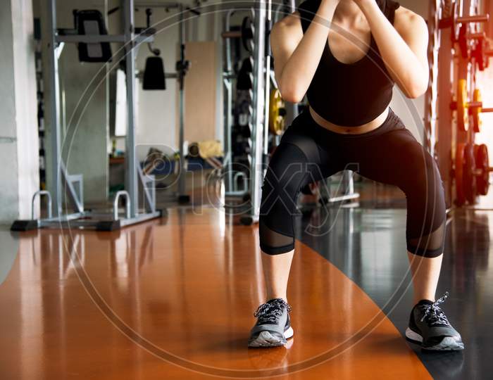 Fitness Woman Doing Squat Workout For Fat Burning And Legs Strength In Fitness Sports Gym With Sports Equipment In Background. Beauty And Body Build Up Concept. Sports Club And Aerobic Theme.