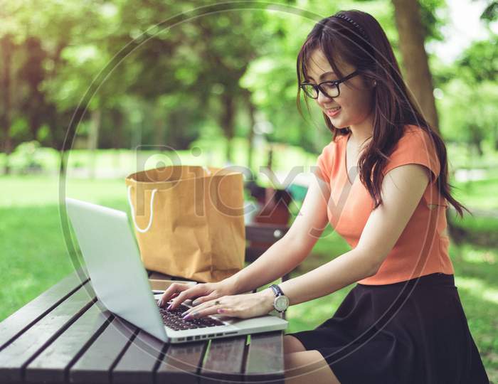 Asian Woman Using And Typing On Laptop Keyboard In Outdoors Park. Woman Chatting To Her Friends On Social Network. People And Lifestyle Concept. Nature And Technology Theme.