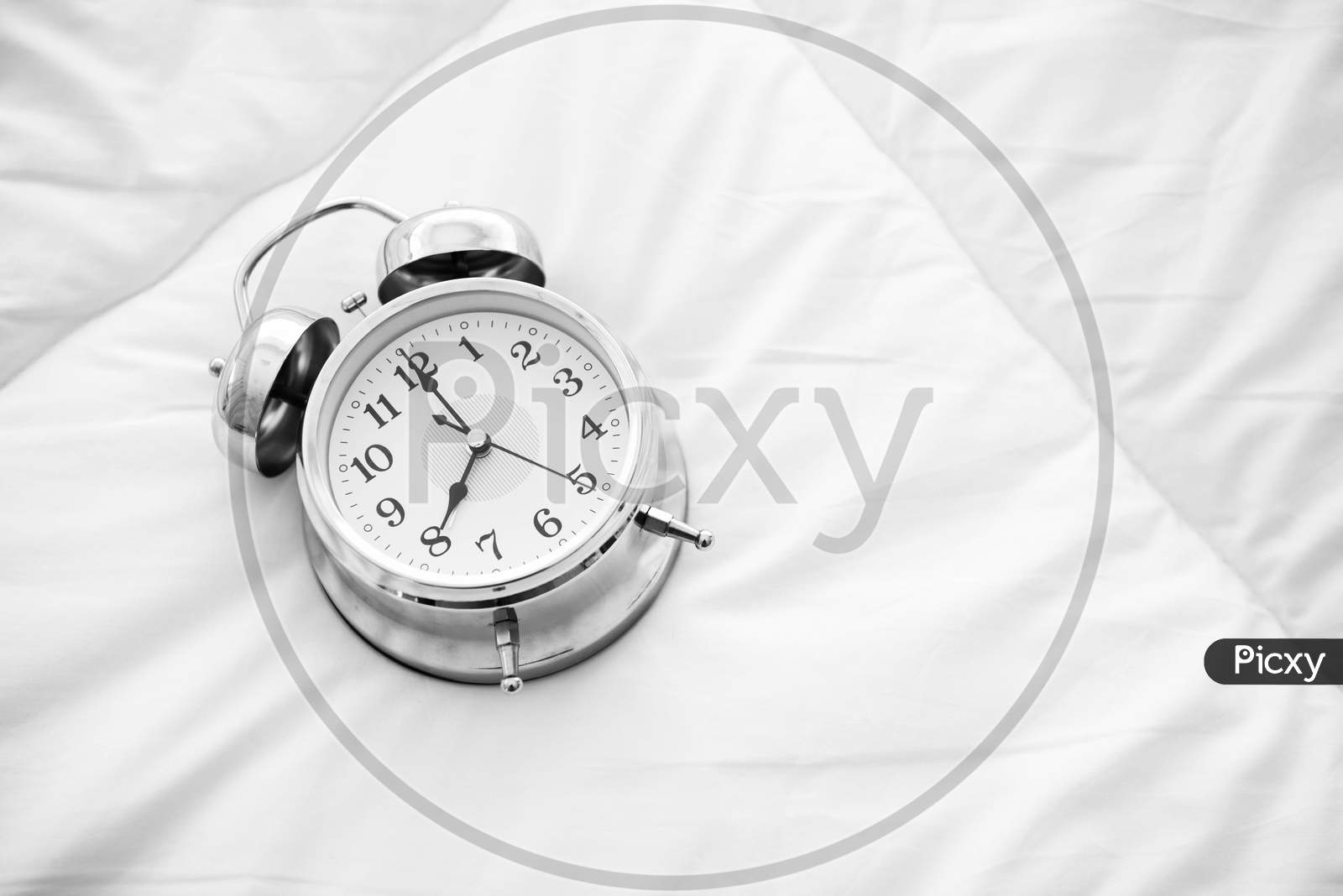 Ringing Alarm Clock On White Bed Sheet. Top View Of Object. 8 O Clock Setting Up