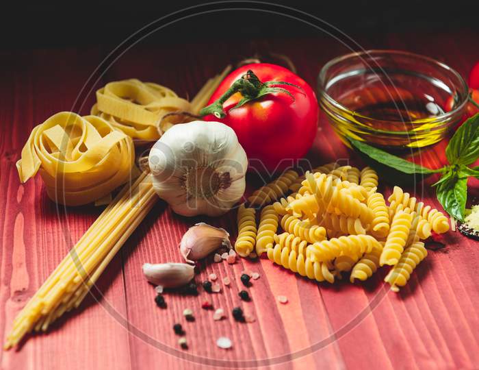 Tasty Appetizing Italian Spaghetti Pasta Ingredients For Kitchen Cuisine With Tomato, Cheese Parmesan, Olive Oil, Fettuccine And Basil On Wooden Brown Table. Food Italian Recipe Homemade. Top View