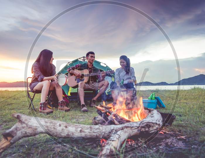 Group Of Travelers Camping And Doing Picnic And Playing Music Together. Mountain And Lake Background. People And Lifestyle. Outdoors Activity And Leisure Theme. Backpacker And Hiker. Dawn And Twilight