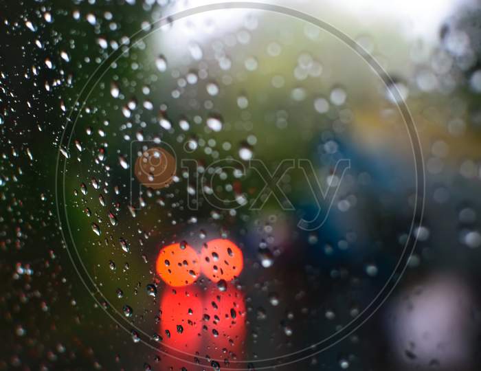 Rain Drops On A Glass With Visible Red Lights Of A Car Through The Glass