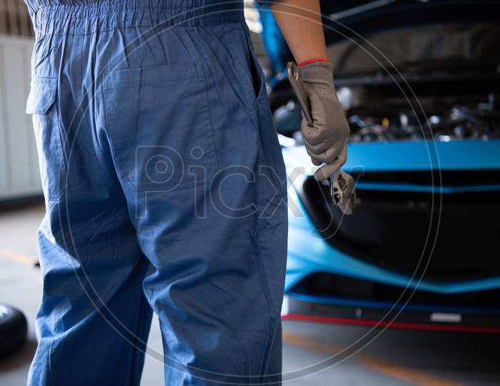 Car Mechanic Holding Wrench For Fixing To Customer Claim Order In A Auto Repair Garage Workshop. Engine Repair Service. People Occupation And Business Job. Automobile Industry Technical Maintenance