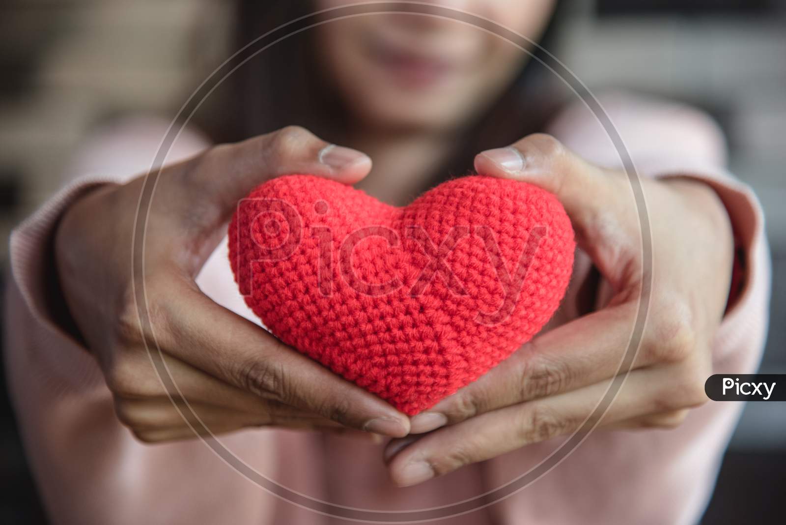 Big Red Yarn Heart Holding And Giving To Front By Woman Hand. Love And Affection In Valentines Day Concept. Romantic Object And Health Care.