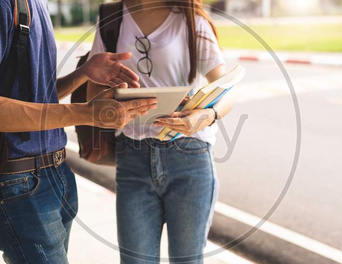 Close Up Of Two College Student Discussion With Tablet. Girl Holding Books Talking To Boy In University Or School. Education And Lifestyle Learning. Technology And Self Learning Concept