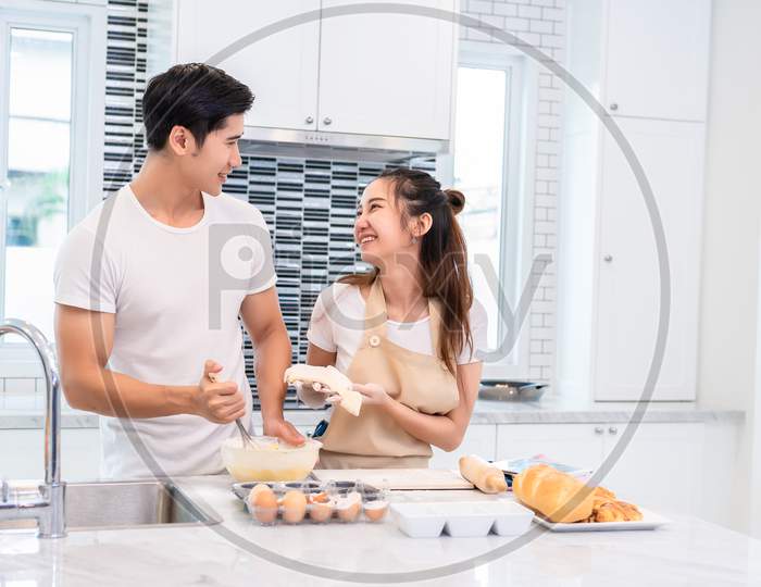 Asian Couples Cooking And Baking Cake Together In Kitchen Room. Man And Woman Looking To Each Other At Home. Love And Happiness Concept Sweet Honeymoon And Valentine Day Theme
