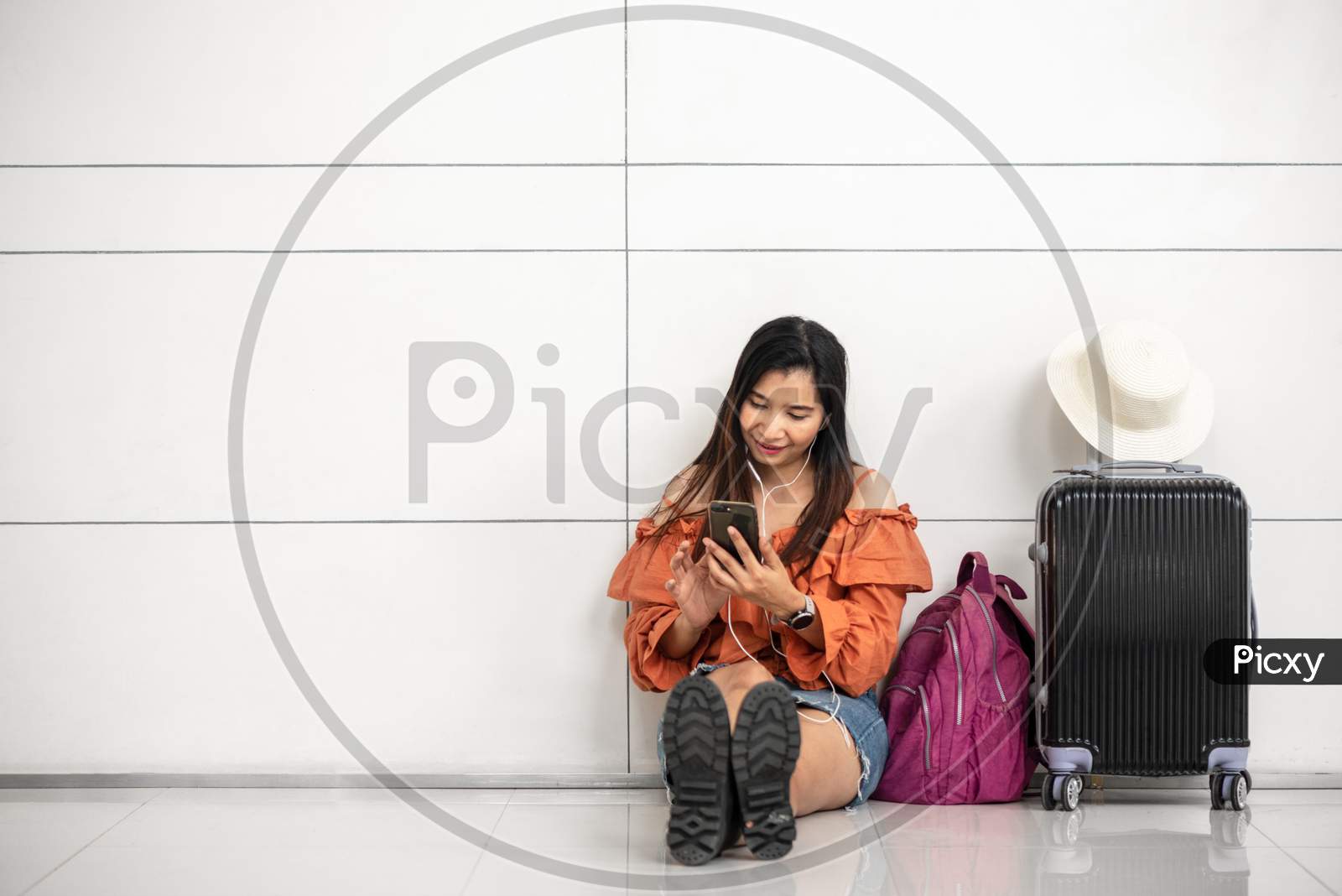 Asian Female Traveler Waiting For Flight And Using Smart Phone Outside Lounge In Airport. Travel And People Lifestyle Concept. Transportation And Passenger Theme.