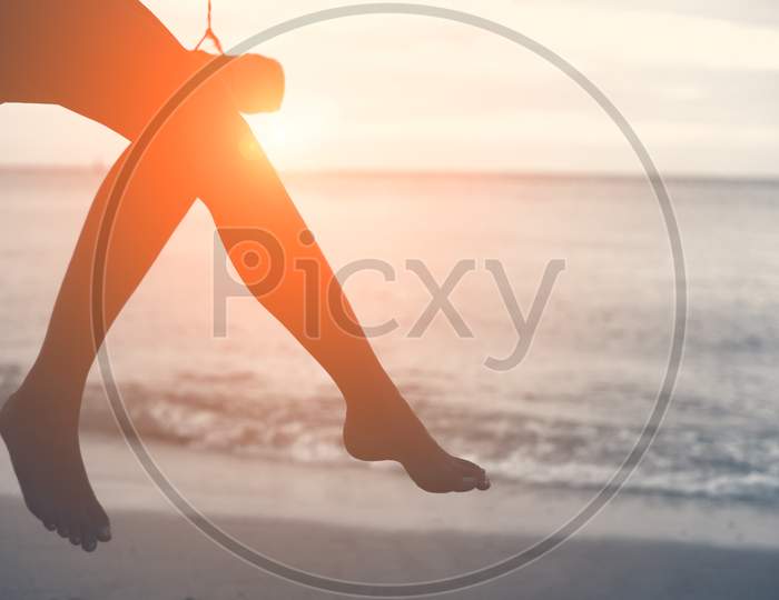 Woman Legs At Beach On Wooden Swing With Sunset. Single Woman Concept. People And Lifestyle Concept. Lonely And Sadness Concept. Beach And Sea Theme. Finding Soulmate Theme. Copy Space On Right