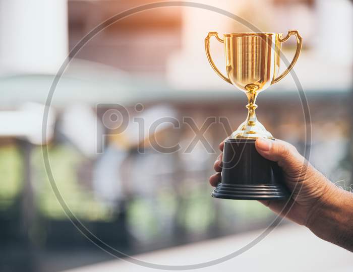 Champion Golden Trophy For Winner In Hand Background. Success Achievement Concept. Sport And Cup Award Theme. Best Business Entrepreneur And Startup Award And Prize. First Place On Final Competition