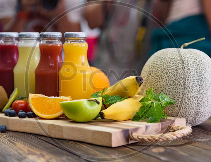 Fresh Fruits And Juice Bottle On Table. Food And Drink Concept. Healthy Food And Vitamins C Theme. Crowd People In Background