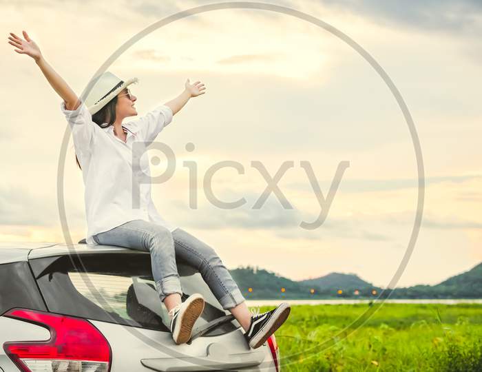 Happy Asian Woman Spread Arms Widely And Breathed Fresh Air With Happiness Mood In Evening After Sunset On Car Roof. People Lifestyle In Long Vacation Trip Concept. Outdoors Nature And Transportation