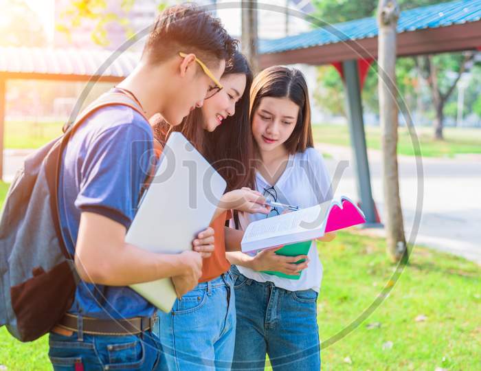 Three Asian Young Campus People Tutoring And Preparing For Final Examination In University. Education And Learning Concept. Friendship And Relation Ship Concept. College And Outdoors Theme.
