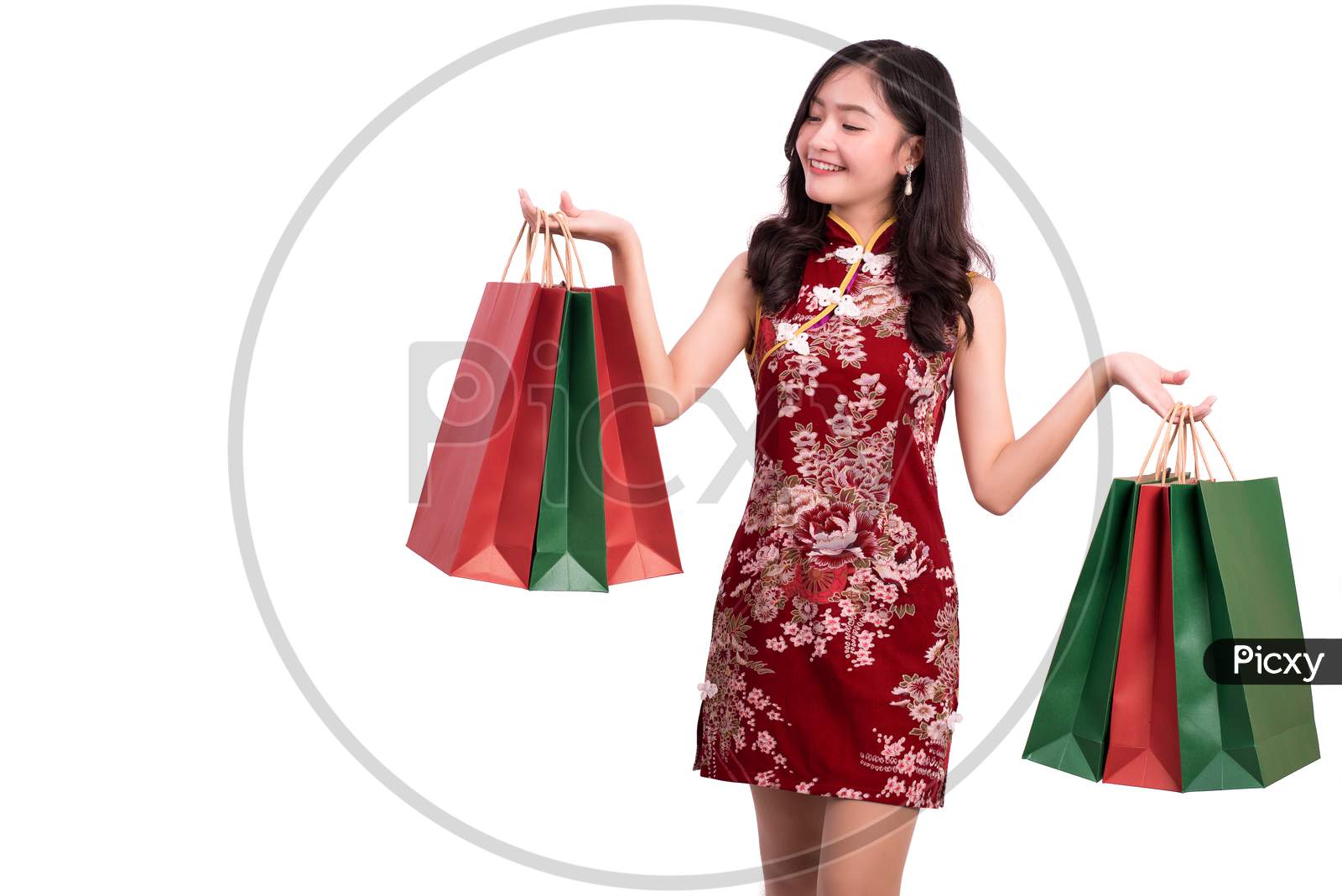 Young Asian Beauty Woman Wearing Cheongsam And Holding Red And Green Shopping Bags Gesture In Chinese New Year Festival Event On Isolated White Background. Holiday And Lifestyle Concept. Qipao Dress