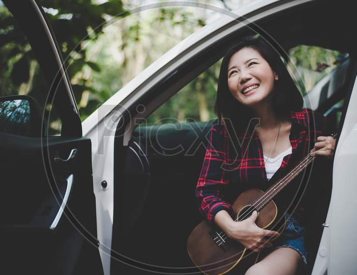 Beauty Asian Woman Smiling And Having Fun At Outdoors Summer With Ukulele In White Car. Traveling Of Photographer Concept. Hipster Style And Solo Woman Theme. Lifestyle And Happiness Life Theme.